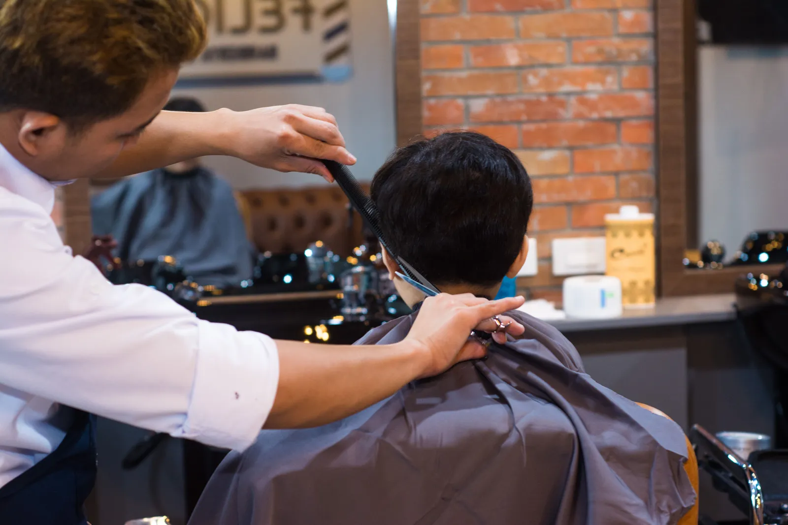 Barbeiro a cortar o cabelo de um cliente à tesoura